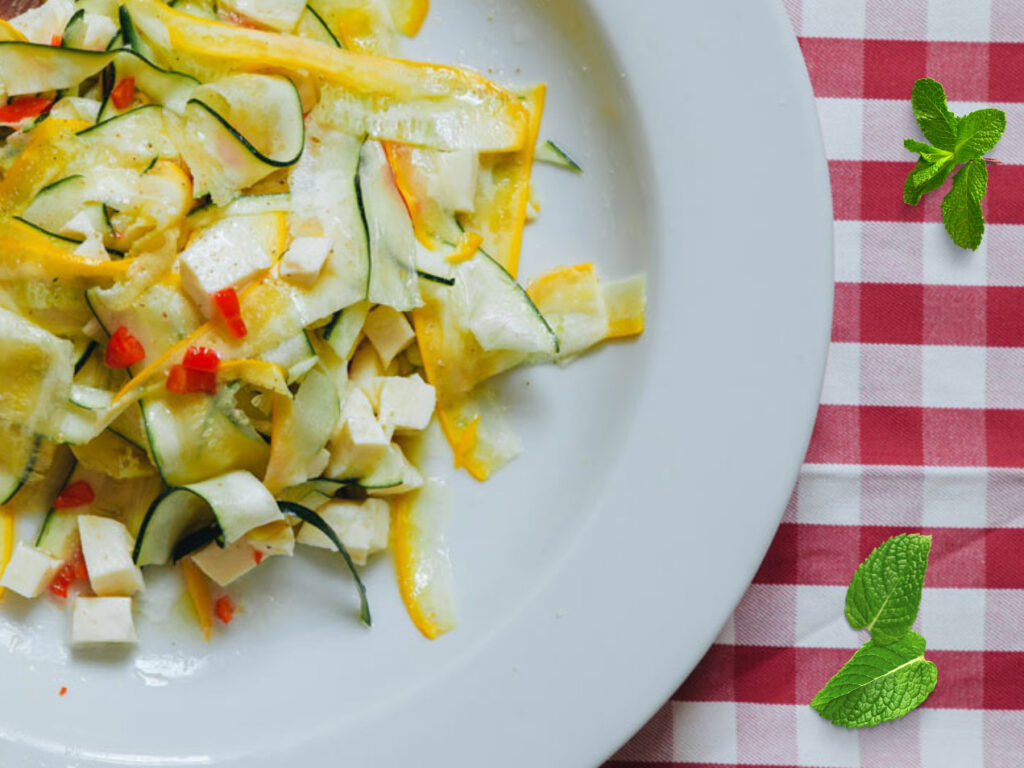 Zucchinis salad with yellow and green zucchinistre, mozzarella and chilli on a white plate